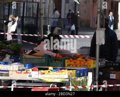 Rom, Italien. April 2020. Ein Anbieter mit Gesichtsmaske verkauft Früchte auf einem Markt in Rom, Italien, 6. April 2020. Die Coronavirus-Pandemie hat 16.523 Leben im eingesperrten Italien gefordert, was die Gesamtzahl der Infektionen, Todesfälle und Erholungen seit Beginn der Pandemie auf 132.547 brachte, nach neuen Daten, die vom Zivilschutzministerium des Landes am Montag veröffentlicht wurden. Credit: Augusto Casasoli/Xinhua/Alamy Live News Stockfoto