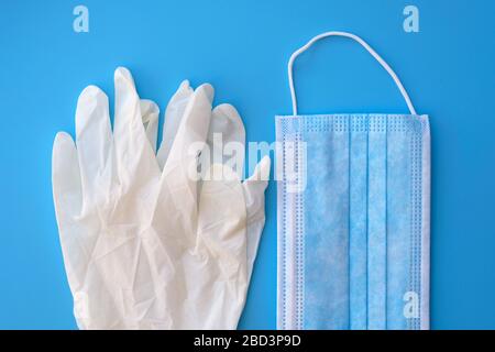 Blaue Gesichtsmaske und nicht sterile Einweghandschuhe. Weiße Nitrilhandschuhe und eine Gesichtsmaske auf blauem Hintergrund in der Draufsicht. Schutz vor dem c