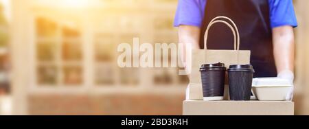 Der Lieferer hält Lebensmittelboxen und Kaffee mit Gummihandschuhen. Online-Shopping und kostenlose Lieferung zu Hause. Soziale Distanzierung und Aufenthalt zu Hause bleiben Sie sicher. Stockfoto