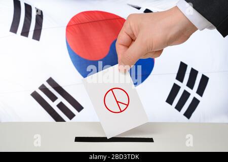 Südkoreanisches Wahlkonzept. Die Hand eines Mannes mit einer Wahlurne in einer Wahlurne vor dem Hintergrund einer koreanischen Flagge Stockfoto