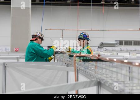 Detroit, Michigan, USA. April 2020. Arbeiter bauen ein Notarztkrankenhaus im TCF-Kongresszentrum auf. Das Krankenhaus mit 1.000 Betten wird Covid-19-Patienten versorgen. Die Pipefitter installieren ein Sauerstoffversorgungssystem. Kredit: Jim West/Alamy Live News Stockfoto