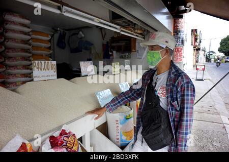 Antipolo City, Philippinen - 4. April 2020: Mann mit improvisierter persönlicher Schutzausrüstung und Gesichtsmaske kauft während des Lockdowns Reis aus einem Laden Stockfoto