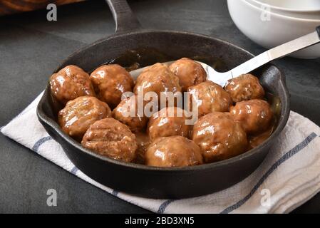 Schwedische Fleischbällchen mit brauner Gravy in einem Gusseisen-Skillet und einem Servierlöffel Stockfoto