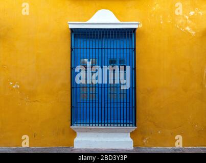 Ein blaues Fenster an einer gelben Wand, eine bunte Fassade im historischen Stadtzentrum von Campeche, Yucatan-Halbinsel, Mexiko. Stockfoto