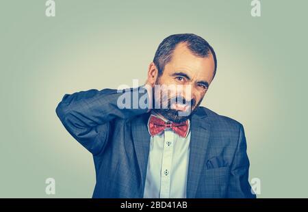 Reifer Mann mit Nackenschmerzen, isoliert auf hellgrüngelbem Gradientenwandhintergrund. Negative Gesichtsausdruck des Menschen Stockfoto