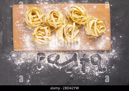 Verschiedene italienische hausgemachte rohe, ungekochte Pasta Spaghetti und Tagliatelle mit Mehl auf Holzbrett über schwarzem Texturhintergrund. Flaches Lay Stockfoto
