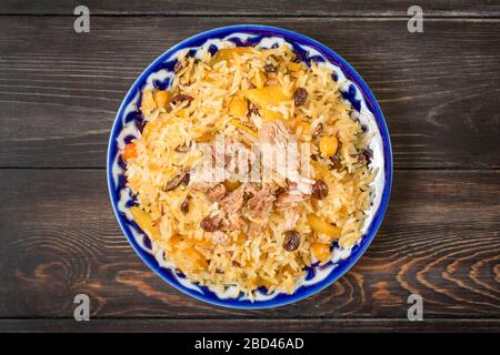 Nationale Küche - usbekischer Pilaf mit Fleisch in Platte mit traditionellem Muster auf dunklem Holztisch Top View Flat Lay Ramadan, Nowruz Urlaubskonzept Stockfoto