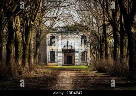 Nahaufnahme einer von Bäumen gesäumten Feldstraße, die zu führt Das Portal eines alten und verlassenen Klosters Stockfoto