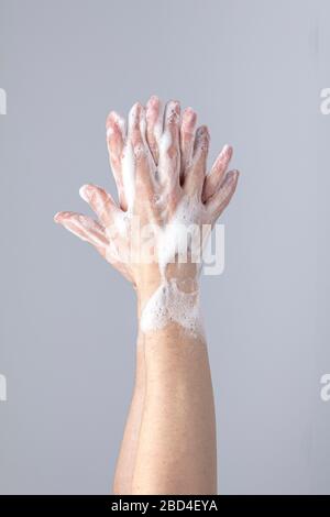 Weiße Menschenhände waschen sich mit grünem Schaum Marseilles Seife isoliert vor einem grauen Hintergrund mit strukturierenden Lichtern und Schatten Stockfoto