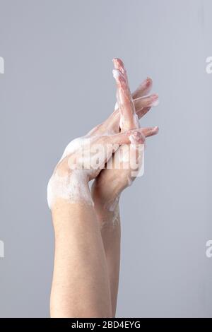 Weiße Menschenhände waschen sich mit grünem Schaum Marseilles Seife isoliert vor einem grauen Hintergrund mit strukturierenden Lichtern und Schatten Stockfoto