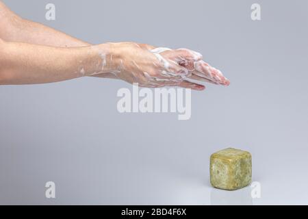 Weiße Menschenhände waschen sich mit grünem Schaum Marseilles Seife isoliert vor einem grauen Hintergrund mit strukturierenden Lichtern und Schatten Stockfoto