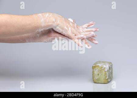 Weiße Menschenhände waschen sich mit grünem Schaum Marseilles Seife isoliert vor einem grauen Hintergrund mit strukturierenden Lichtern und Schatten Stockfoto