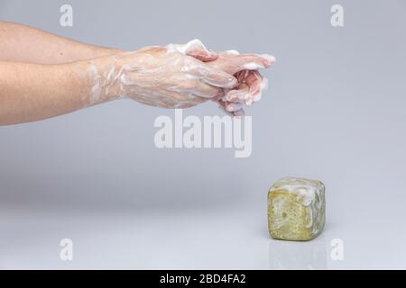 Weiße Menschenhände waschen sich mit grünem Schaum Marseilles Seife isoliert vor einem grauen Hintergrund mit strukturierenden Lichtern und Schatten Stockfoto