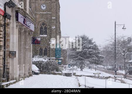 Schneebedecktes winterliches Stadtbild (schneite, schneebedeckte Hochstraße, Kirche, Geschäfte und Straße im malerischen Stadtzentrum) - The Grove, Ilkley, Yorkshire, England, Großbritannien. Stockfoto