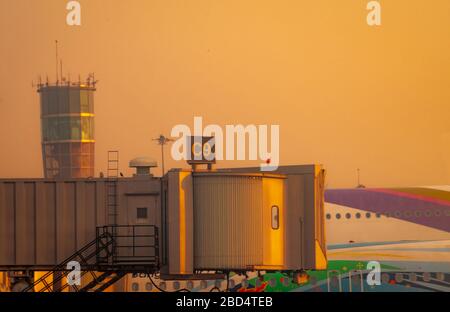 Kommerzielle Flugzeuge, die auf der Jet-Brücke für den Passagierabflug am Flughafen geparkt wurden. Flugpassagierbrücke mit goldenem Himmel in der Nähe angedockt Stockfoto