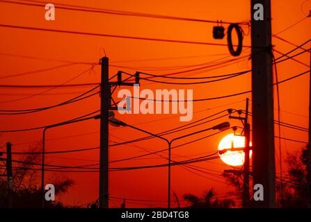 Elektrische Pole und Übertragungsleitungen am Abend. Elektrizitätspylone mit Kabelanschluss und Straßenlaterne bei Sonnenuntergang. Energie und Energie in der ländlichen Stadt Stockfoto