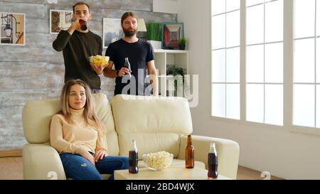 Eine Gruppe von Freunden, die auf der Couch sitzen und nach Pizza greifen, während sie im Wohnzimmer fernsehen. Stockfoto