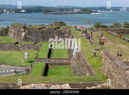 Die Leute versammeln sich auf einem Abschnitt des Dutch Fort (1588) in Galle in Sri Lanka, das einen Cricket-Platz überblickt, wo ein Spiel gespielt wird. Stockfoto