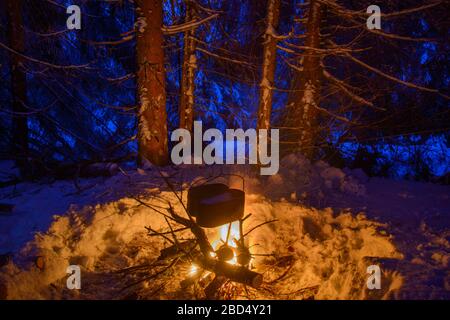 Szene aus Winterreisen. Zwei schwarze Töpfe heizen unter großem Feuer. Das Lagerfeuer ist von schneebedeckten Bäumen umgeben. Funken Spuren sind im i zu sehen Stockfoto