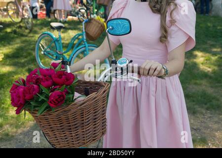 Mädchen im Retrokleid mit einem Blumenkorb auf dem Fahrrad. Menschen Stockfoto