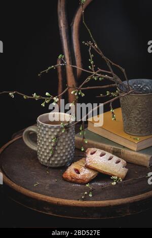 Eine Tasse Tee und hausgemachte Brötchen mit Büchern und einige blühende Baumzweige auf einem Vintage-Stuhl Stockfoto