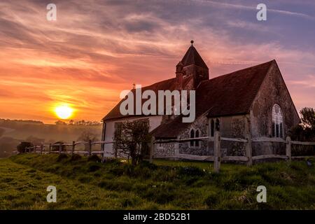 Sonnenuntergang an der abgelegenen St Hubert's Church in Idsworth, South Downs National Park, UK mit einem dramatischen orange, lila und blauen Himmel Stockfoto