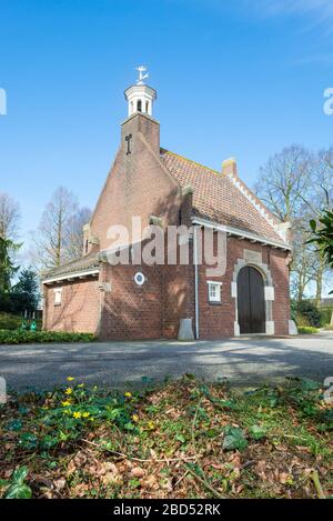 Malerische kleine Kirche auf einem Friedhof in den Niederlanden. Holländischer Text an der Wand bedeutet: "Wer an mich glaubt, wird leben, auch wenn er gestorben ist." Stockfoto