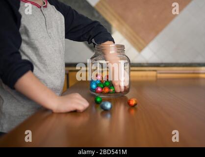 Das Kind nimmt farbige Pralinen aus dem durchsichtigen Glas in der Küche Stockfoto