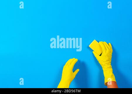 Hände in gelben Handschuhen mit Schwamm auf blauem Hintergrund. Reinigung, Desinfektion von zu Hause Stockfoto