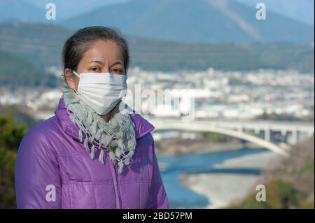 Schöne Frau mittleren Alters mit einer weißen Maske zum Schutz vor Coronavirus COVID-19 (SARS-COV-2) und anderen ansteckenden Krankheiten. Stockfoto