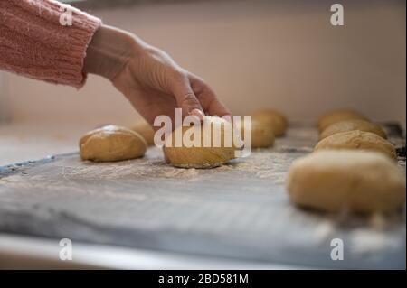 Weibliche Hand, die Sauerteigkugeln auf eine bemehlte Oberfläche auf die Küchenecke legt. Stockfoto