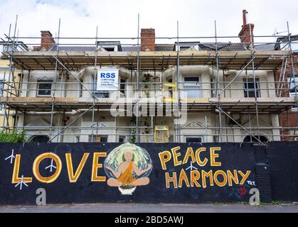 Hausfassade in Gerüsten für Renovierungsarbeiten, die von vor Ort Fechten mit Liebe, Frieden und Harmonie nach außen gemalt umgeben ist abgedeckt Stockfoto