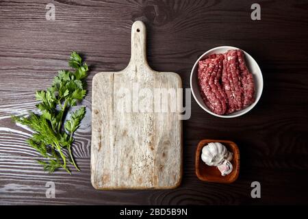 Hackfleisch kochen. Schneidebrett mit frischen Gewürzen auf einem Holztisch, flacher Einlage. Weiße Knoblauchköpfe und Zehen, grüner Dill und Petersilienblätter. Bo Stockfoto