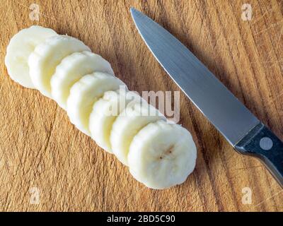 Geschnittene Bananenstücke auf einem Holzhackbrett mit Küchenmesser Stockfoto