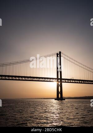 25 April Brücke Silhouette, Lissabon, Portugal. Blick auf den Sonnenuntergang über der Hängebrücke, die den Tejo überquert. Stockfoto