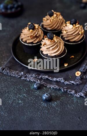 Vier Cupcakes mit Heidelbeere und Haselnuss auf dem Teller dunkel Stockfoto