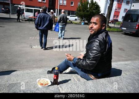 Friedrichshafen, Deutschland. April 2020. 07. April 2020, Baden-Württemberg, Friedrichshafen: Eine bedürftige Person isst auf den Stufen der katholischen Kirche St. Peter Canisius einen Teil Spaghetti-Bolognese. Fast 30 bedürftige Menschen erhalten zur Mittagszeit eine kostenlose Mahlzeit. Neben der städtischen Entkräuselei wurde die Armenspeisung auch von den "Herberge" - einer Einrichtung für Obdachlose - und dem Streetworker-Verein Arkade organisiert. Finanziert wurde das Projekt unter anderem durch Spenden aus der Stadt, dem Landkreis und der Neuolischen Kirche. Viele Einrichtungen, in denen Obdachlose normalerweise empfangen wurden Stockfoto