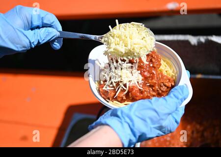 Friedrichshafen, Deutschland. April 2020. 07. April 2020, Baden-Württemberg, Friedrichshafen: Auf dem Platz vor der Kirche St. Peter Canisius geben Helfer den Bedürftigen das kostenlose Essen Spaghetti Bolognese heraus. Fast 30 bedürftige Menschen erhalten zur Mittagszeit eine kostenlose Mahlzeit. Neben der städtischen Diakonie wurde die Armenspeisung auch vom "Hostel" - einer Einrichtung für Obdachlose - und dem Streetworker-Verein Arkade organisiert. Finanziert wurde das Projekt unter anderem durch Spenden aus der Stadt, dem Landkreis und der Neuolischen Kirche. Viele Einrichtungen, in denen Obdachlose n Stockfoto