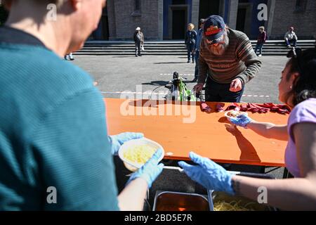 Friedrichshafen, Deutschland. April 2020. 07. April 2020, Baden-Württemberg, Friedrichshafen: Auf dem Platz vor der Kirche St. Peter Canisius geben Helfer den Bedürftigen das kostenlose Essen Spaghetti Bolognese heraus. Fast 30 bedürftige Menschen erhalten zur Mittagszeit eine kostenlose Mahlzeit. Neben der städtischen Diakonie wurde die Armenspeisung auch vom "Hostel" - einer Einrichtung für Obdachlose - und dem Streetworker-Verein Arkade organisiert. Finanziert wurde das Projekt unter anderem durch Spenden aus der Stadt, dem Landkreis und der Neuolischen Kirche. Viele Einrichtungen, in denen Obdachlose n Stockfoto