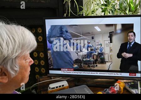 Ältere Frau, die die TV-Nachrichten mit einem Bericht über persönliche Schutzausrüstung und Pflege auf der Intensivstation verfolgt. Stockfoto