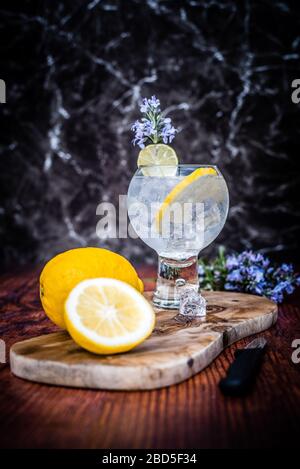 Cold Gin & Tonic Cocktail mit Zitronengarnitur auf Holzhackbrett Stockfoto