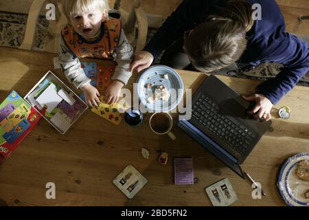 Mutter füttert ihre Kinder beim Essen am Küchentisch während der Arbeit von zu Hause während der Zeit der Selbstisolation - 2020 COVID-19 Coronavirus Pandemie Stockfoto