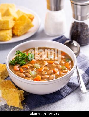 Leckere Bohnensuppe mit Karotten und Sellerie in einer weißen Schüssel und Maisbrot auf der Seite Stockfoto