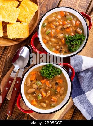 Blick über die Decke von zwei Schalen mit leckerer Bohnensuppe mit Karotten und Sellerie auf einem Holztisch Stockfoto