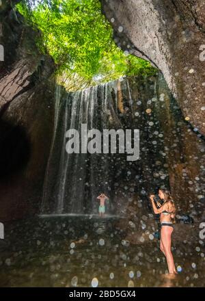 Vertikaler Blick auf Touristen, die in den Tukad Cepung-Wasserfällen in Bali, Indonesien, stehen. Stockfoto