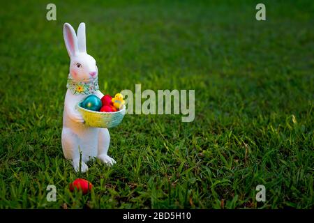 Ein Kaninchen-Souvenir mit Ostern bemalten Eiern auf dem grünen Gras. Kleiner Hase mit Korb. Stockfoto