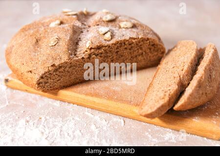 Frisches, hausgemachtes gesundes Brot aus Roggenmehl mit Kürbiskernen auf rustikalem Holzschnittbrett auf Marmor-Arbeitsplatte in heller Küche Stockfoto