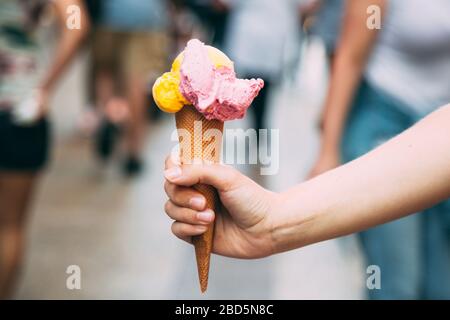 Frau hände ein Eis auf der Straße voller unerkennbarer Menschen, die spazieren gehen Stockfoto