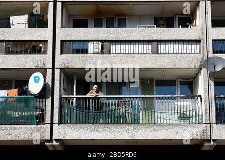 Leith, Edinburgh, Schottland, Großbritannien. April 2020. In der dritten Woche des landesweiten Coronavirus Sperrlebens in Leith geht es weiter, obwohl die Straßen meist verlassen sind und Geschäfte geschlossen sind. Abgebildet; älterer Mann auf Balkon in seiner Wohnung in Kabeln Wynd House Apartmentblock. Stockfoto