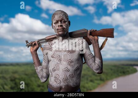 Mit seinem Gewehr und seiner Körperfarbe hoch über dem Omo River, einem Karo-Stamm oder ethnischen Gruppenmitglied, Tumi, Äthiopien. Stockfoto